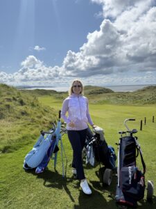 Ballybunion golf course in Ireland. Ashlee holding wine glass with golf carts and sea behind her.